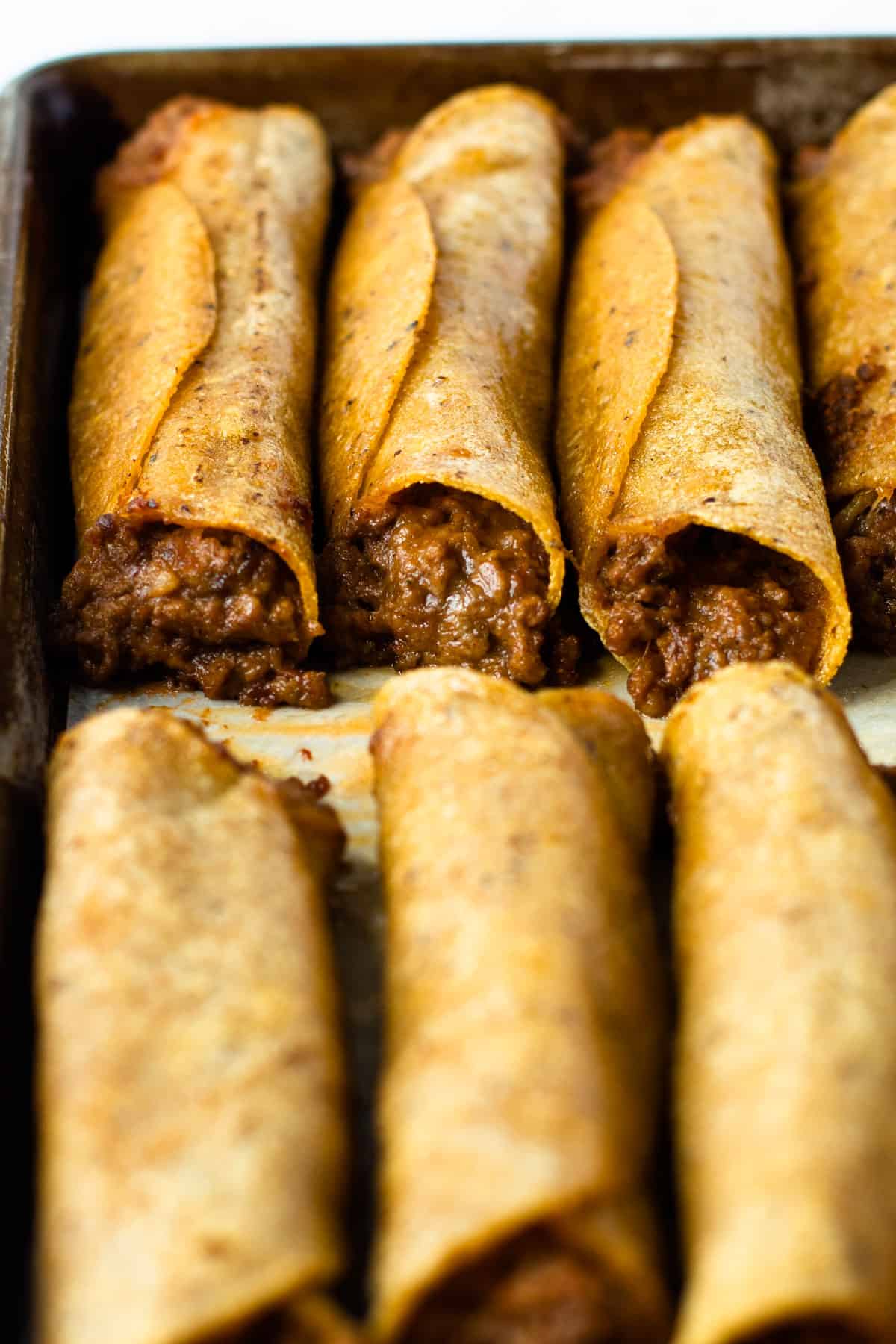Baked taquitos on a sheet pan.