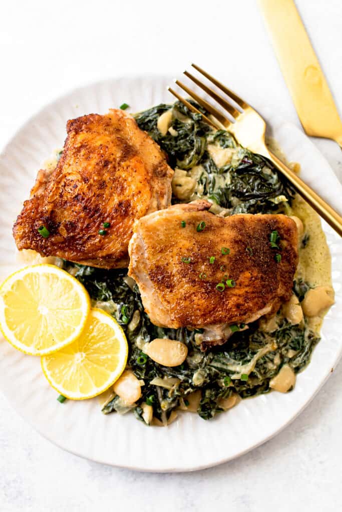 A plate with crispy chicken thighs and lemon greens.
