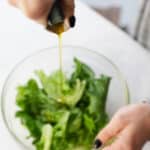 A bottle of olive oil being poured into a salad.