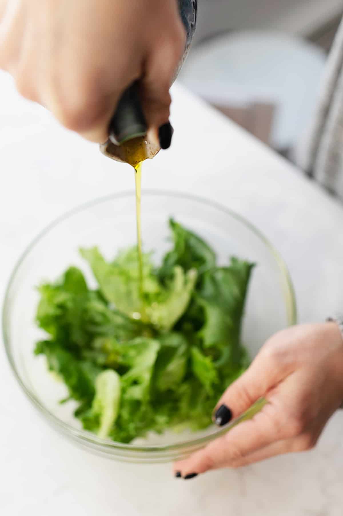 A bottle of olive oil being poured into a salad.