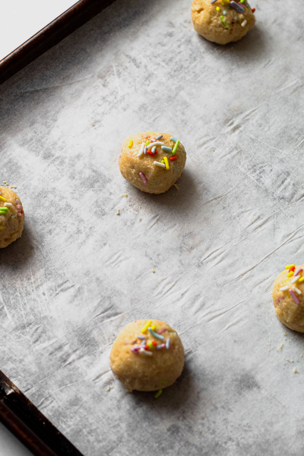 Funfetti cookie dough balls unbaked on a sheet tray.