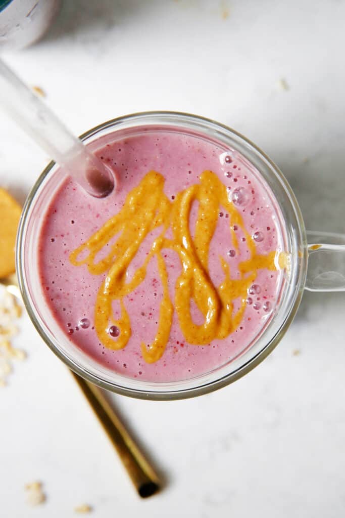 A peanut butter and jelly smoothie in a glass with peanut butter drizzle.