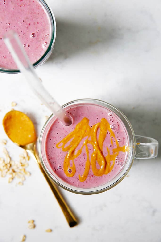 A cup with peanut butter and jelly smoothie and a drizzle of peanut butter.