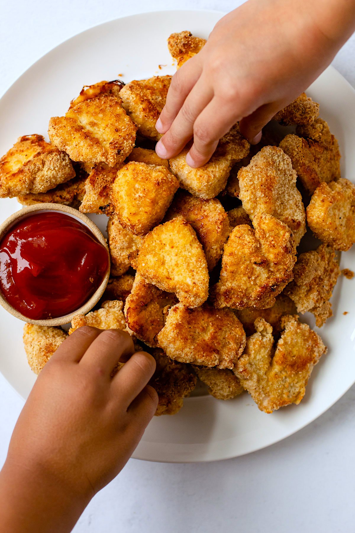 Kids hands grabbing gluten-free chicken nuggets.