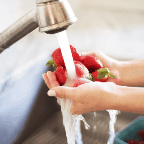 Tap water cleaning strawberries from a sink
