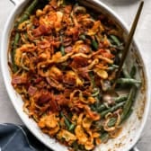 Fully cooked green bean casserole in a white baking dish with a blue napkin underneath and a spoon for serving.