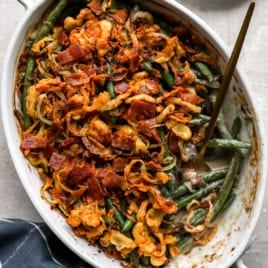Fully cooked green bean casserole in a white baking dish with a blue napkin underneath and a spoon for serving.