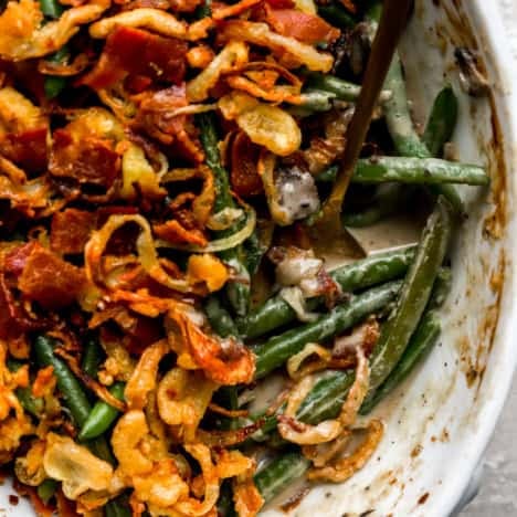 A close up of fully cooked green bean casserole in a white baking dish and a gold spoon for serving.