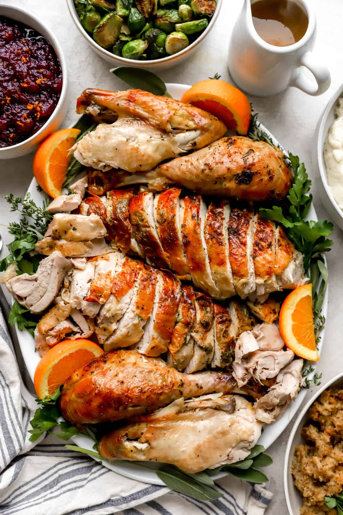 a sliced Thanksgiving turkey presented on a platter with orange slices and greens from above.