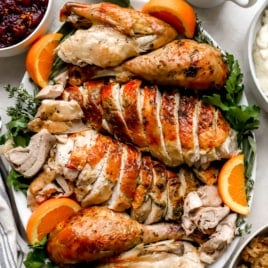 a sliced Thanksgiving turkey presented on a platter with orange slices and greens from above.