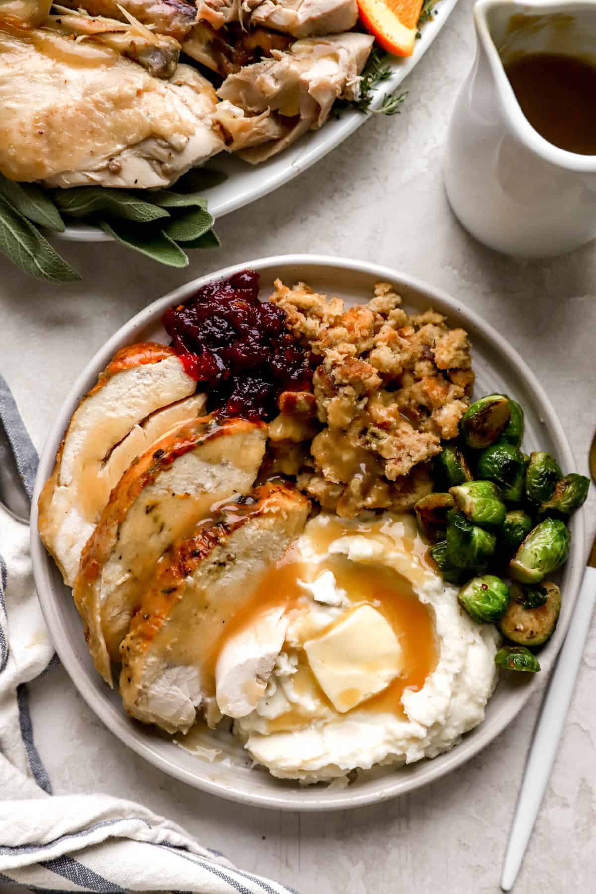 overhead image of a plate piled with a turkey dinner with turkey, cranberry sauce, stuffing, brussels sprouts, and mashed potatoes.