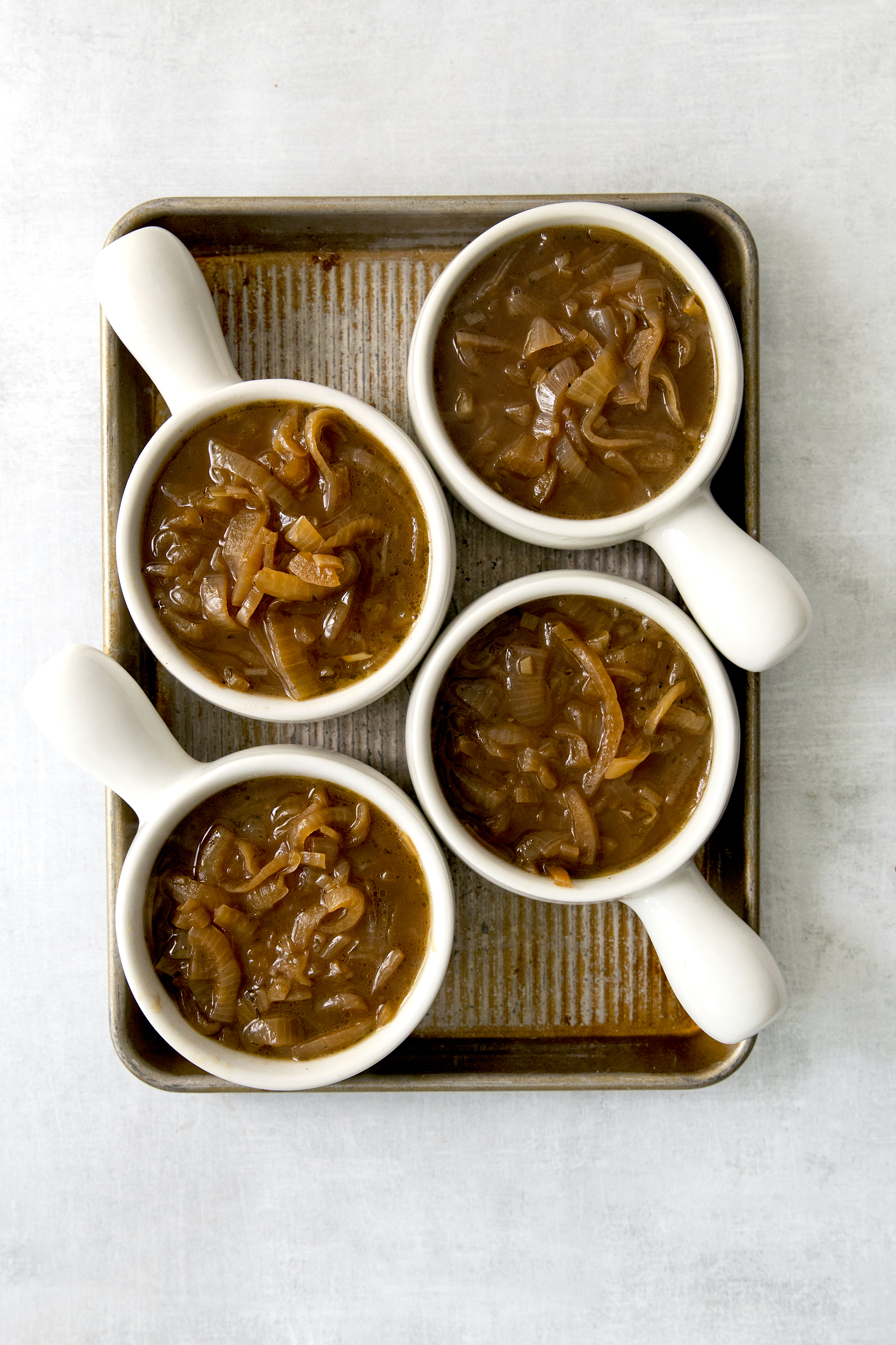 four bowls on a baking sheet filled with french onion soup.
