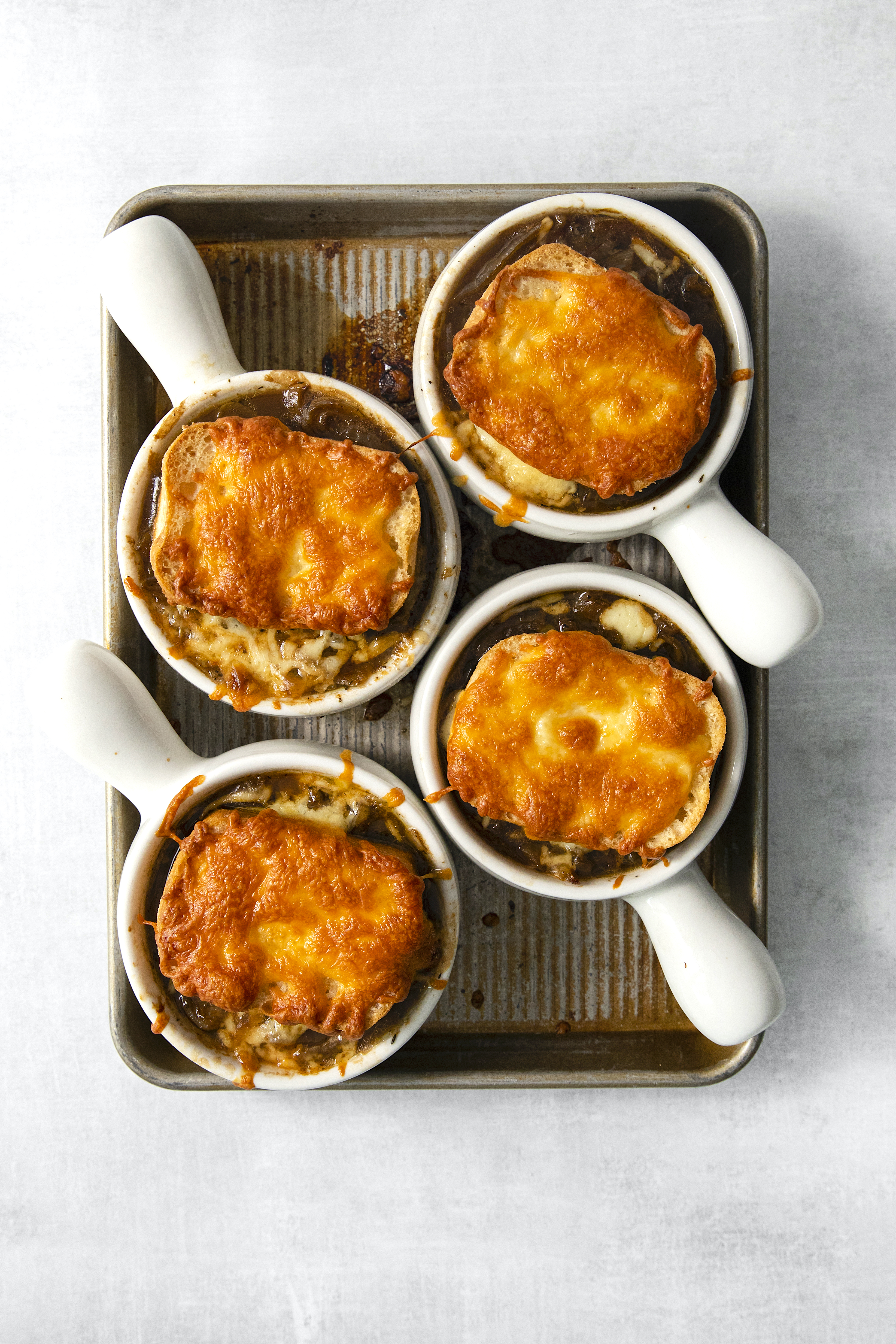 baked, cheesy french onion soup in four white bowls on a baking sheet.