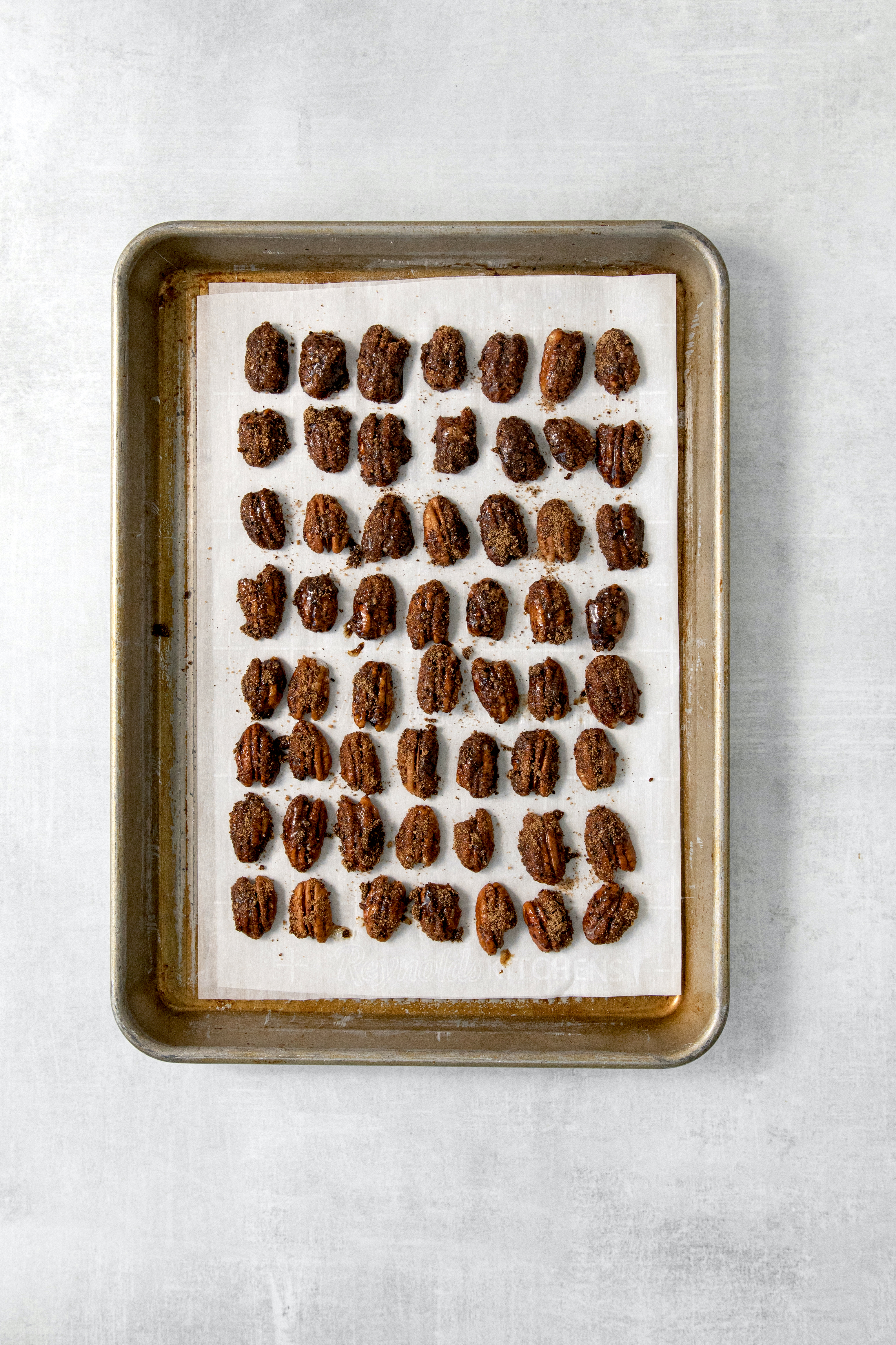 overhead of candied pecans lined on a baking sheet.