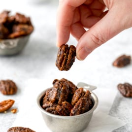 a tin of candy pecans with one being lifted off the top.