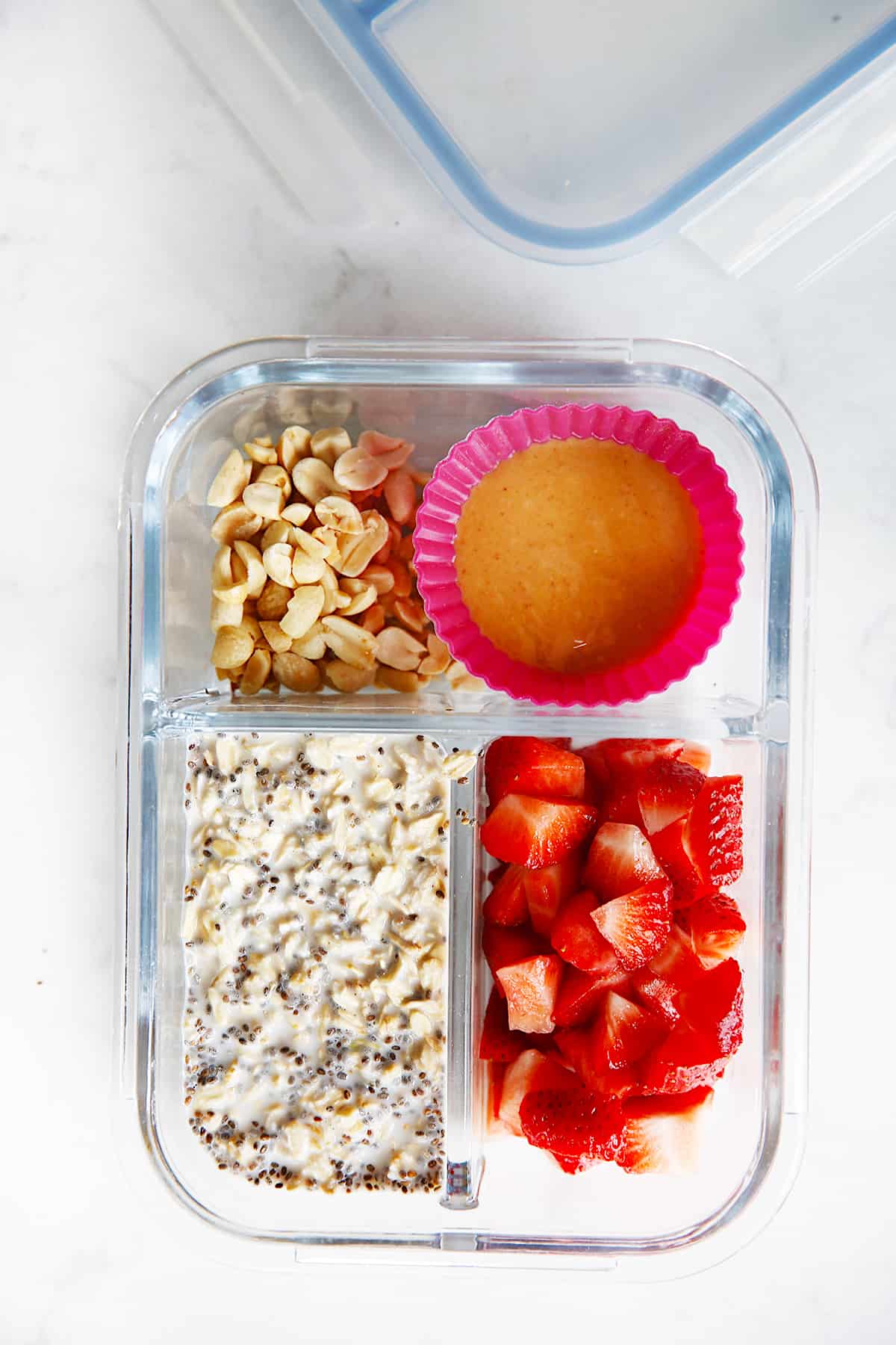 overhead of a container filled with oats, strawberries, peanuts, and nut butter.