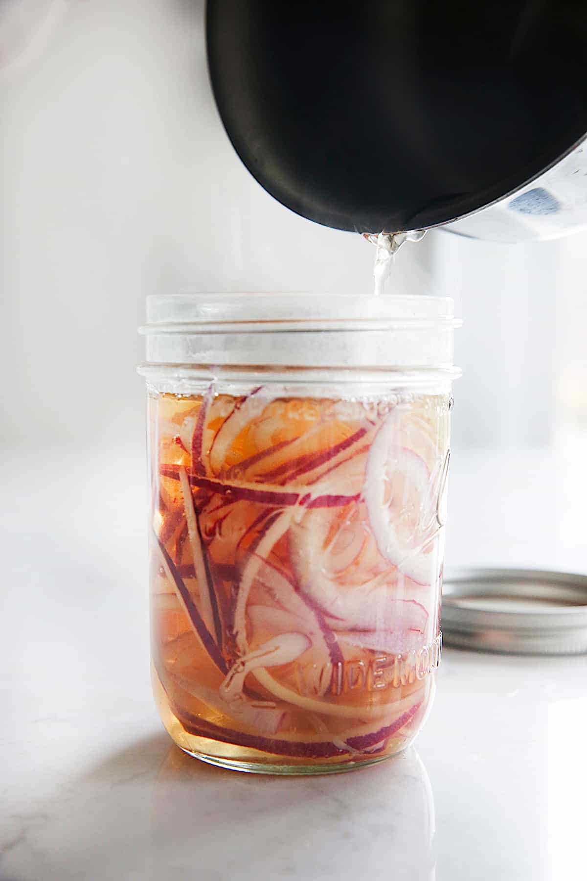 vinegar being poured into a mason jar with red onions.