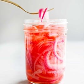 pickled red onions being lifted out of a mason jar with a fork.