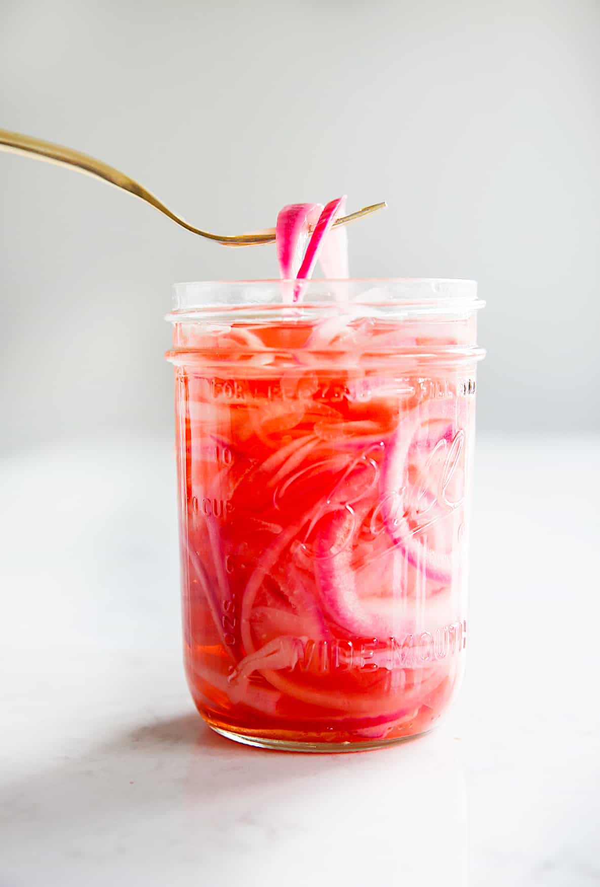 pickled red onions being lifted out of a mason jar with a fork.