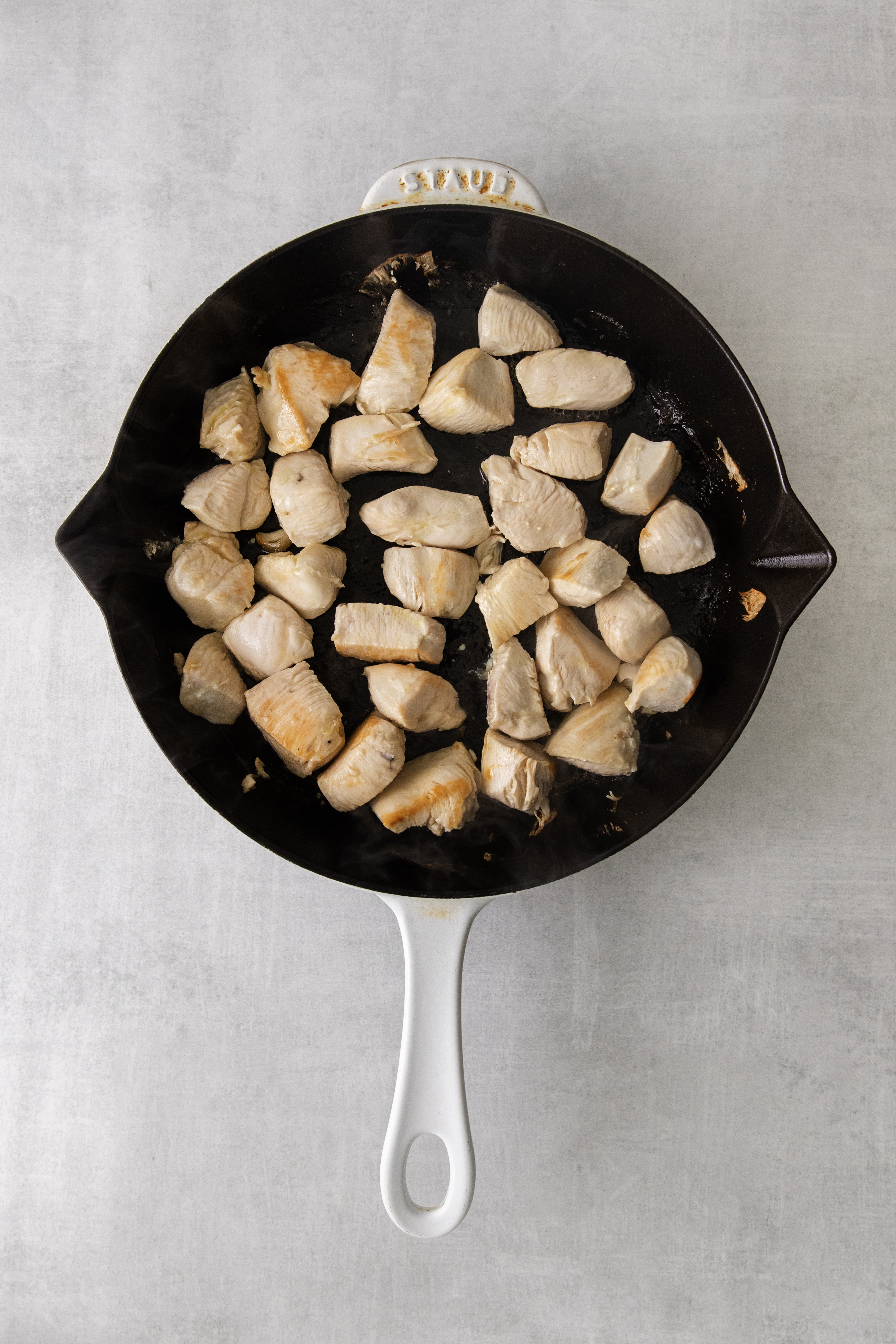 cubes of raw chicken in a skillet.