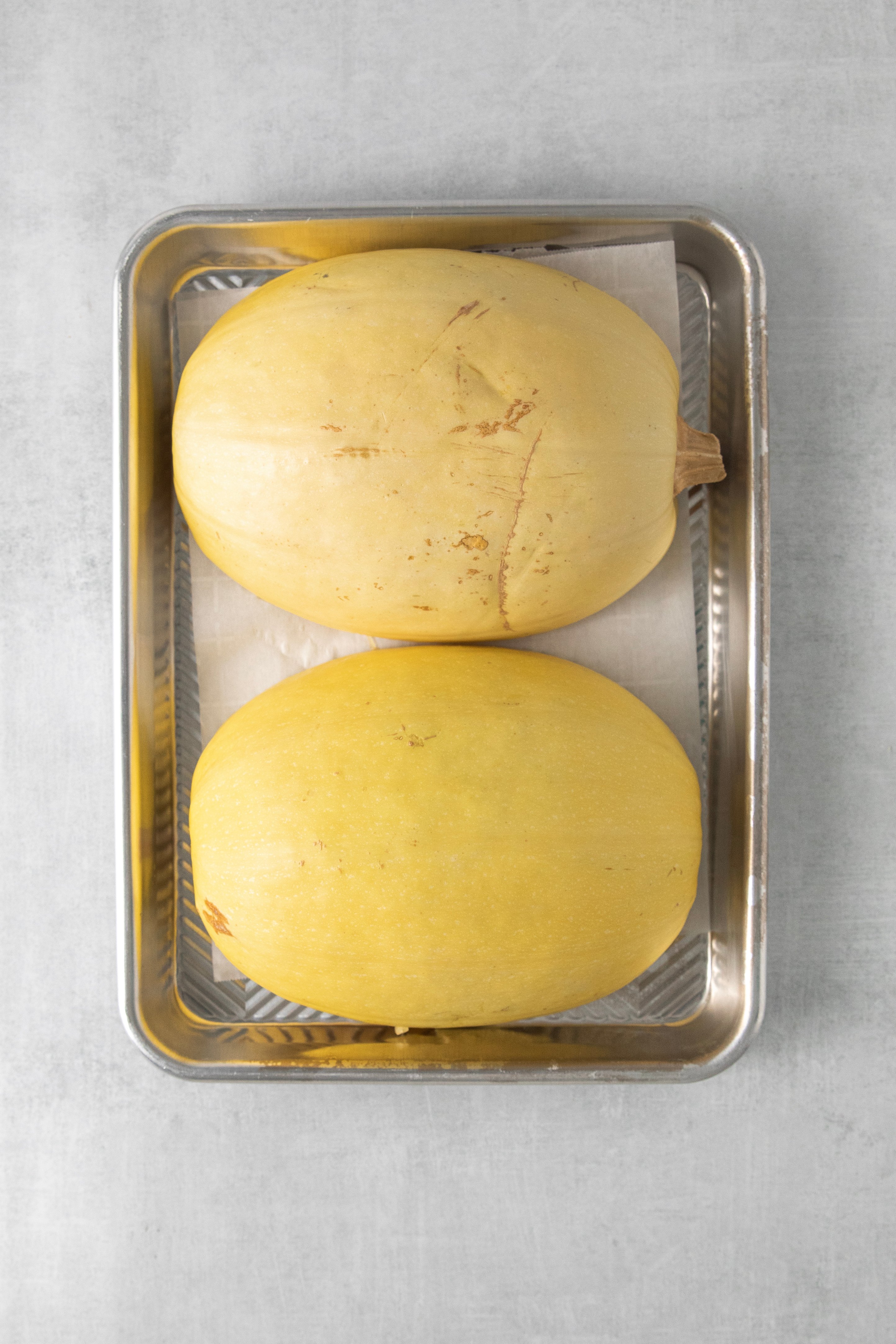 two halves of a spaghetti squash lying facedown on a baking sheet.