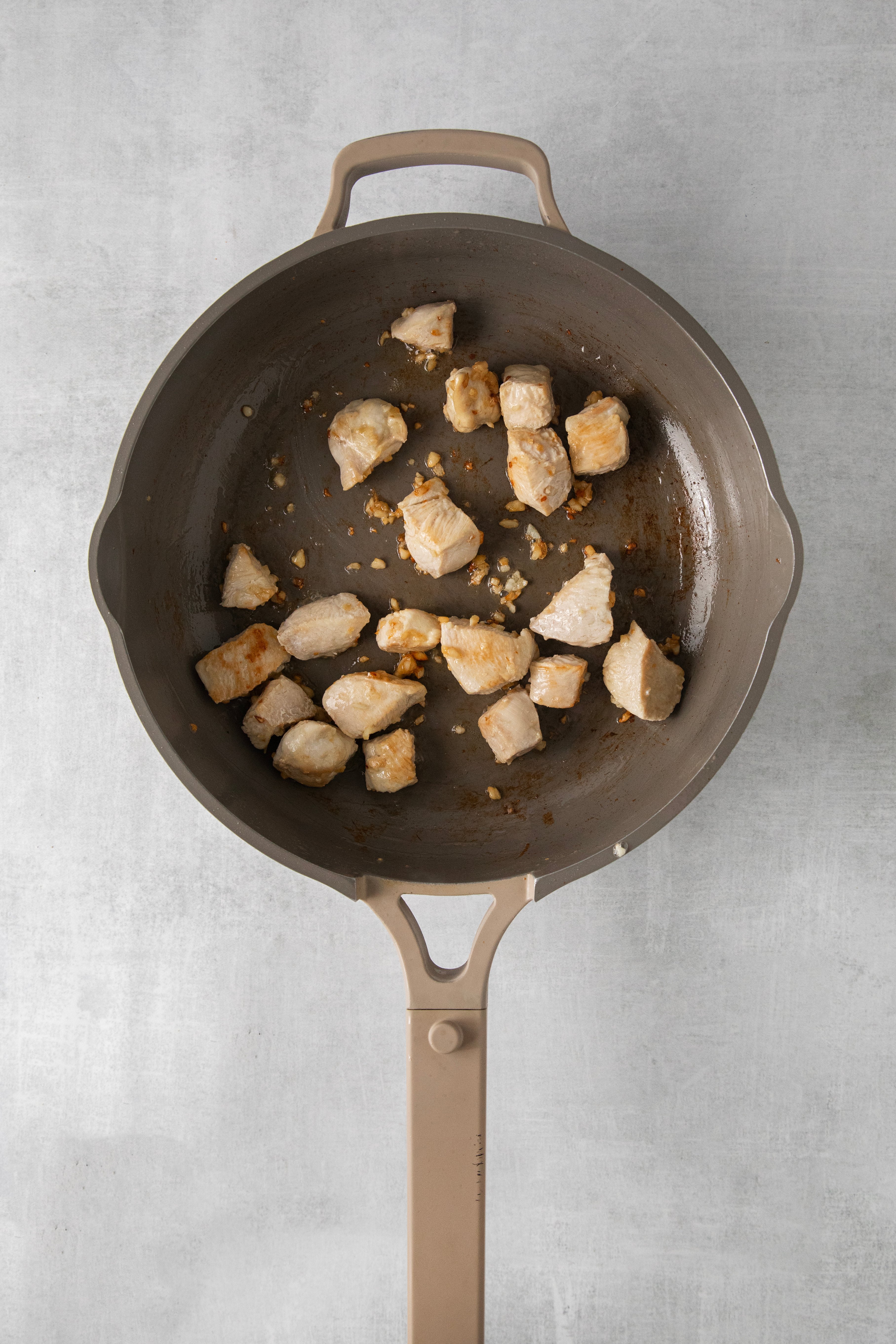 cubes of chicken being seared in a skillet.