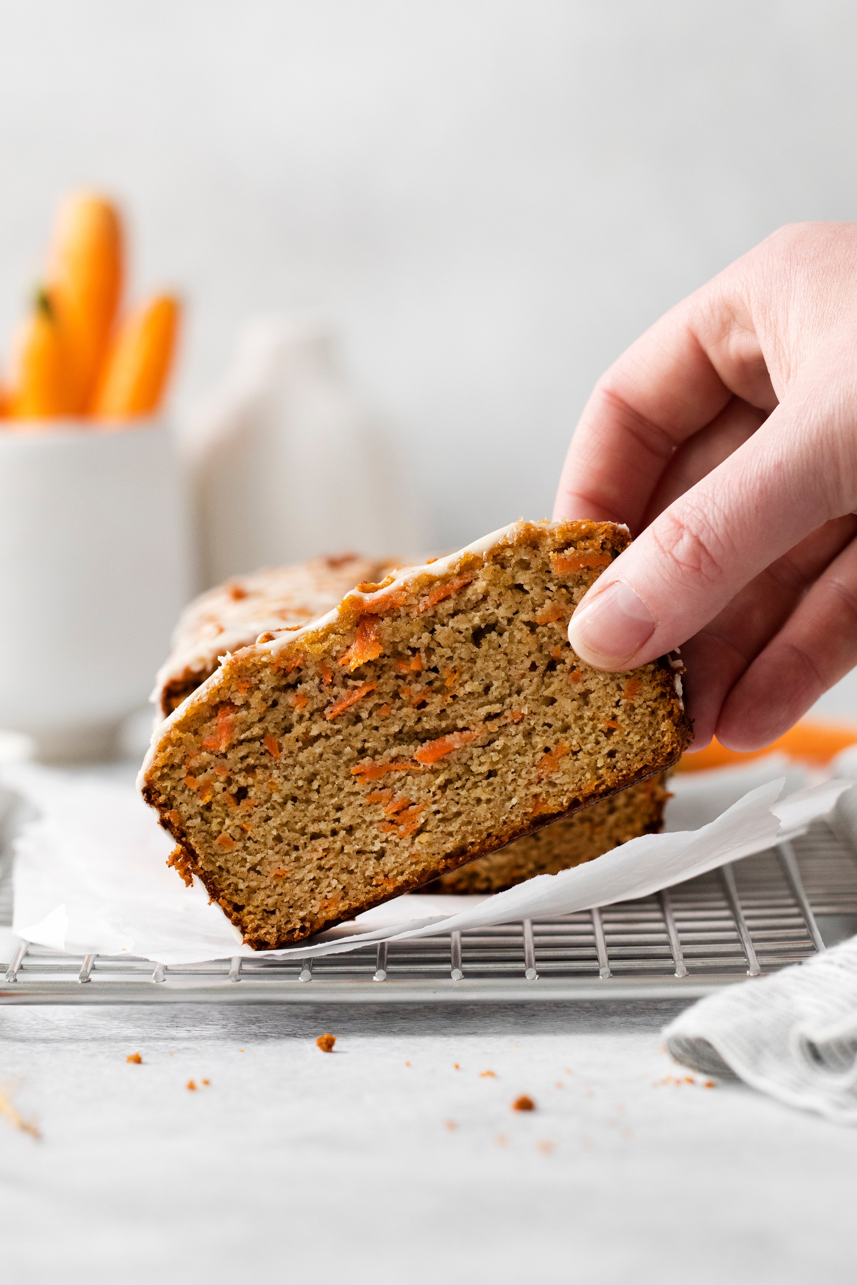 a slice of carrot loaf being lifted off of a cooling rack.