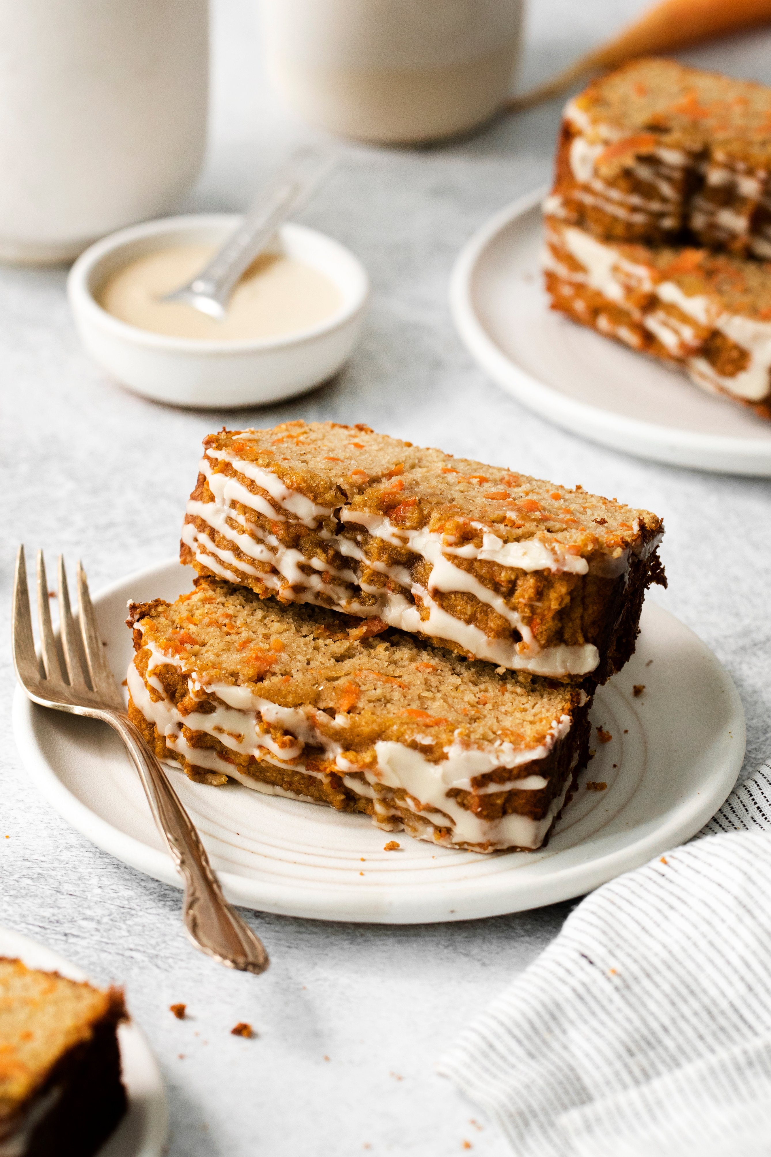 two slices of carrot cake loaf stacked on a plate next to a fork.