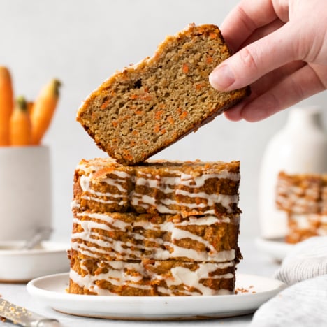 a slice of carrot cake being lifted off of a stack on a plate.