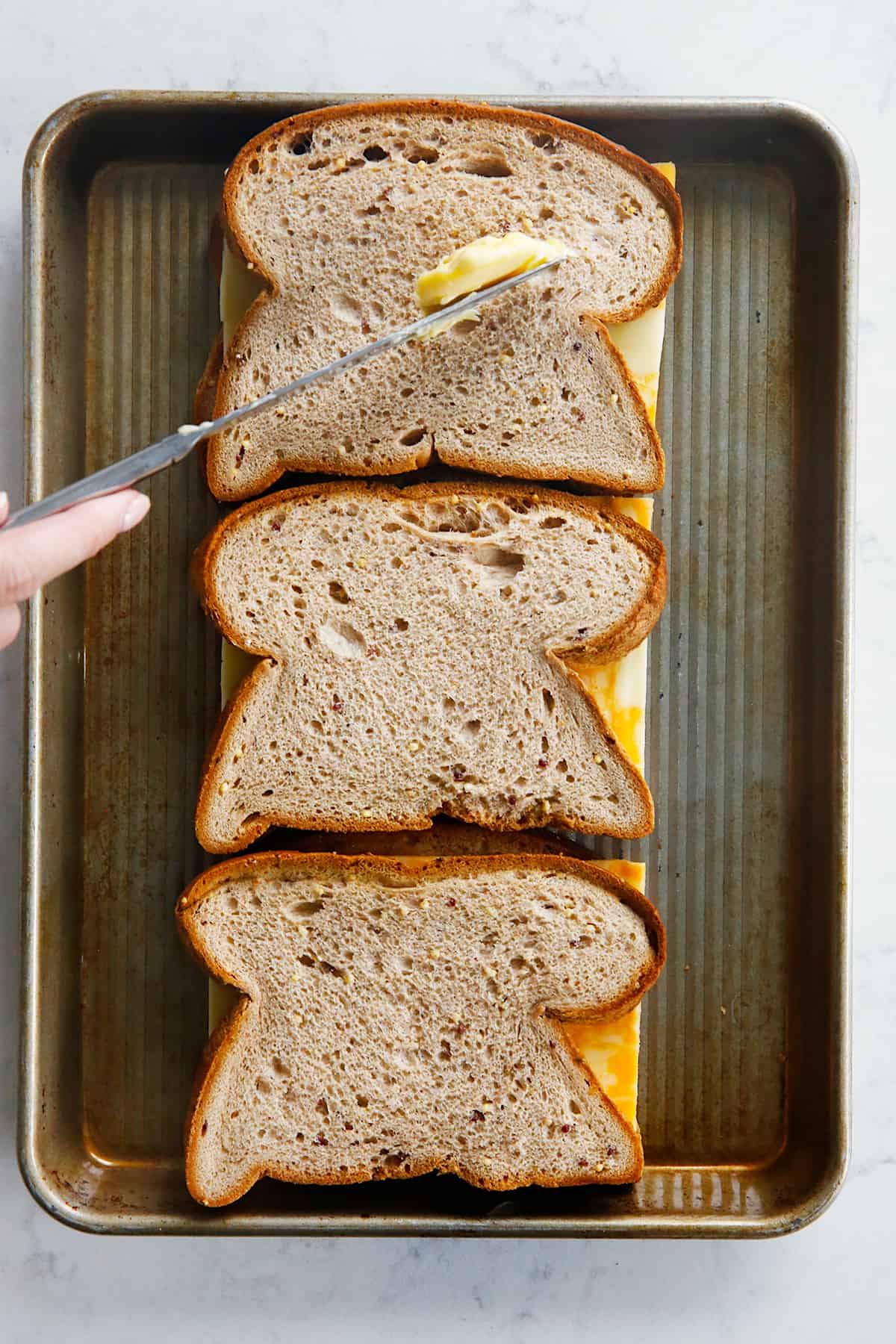 cheese sandwiches on a sheet pan being buttered.