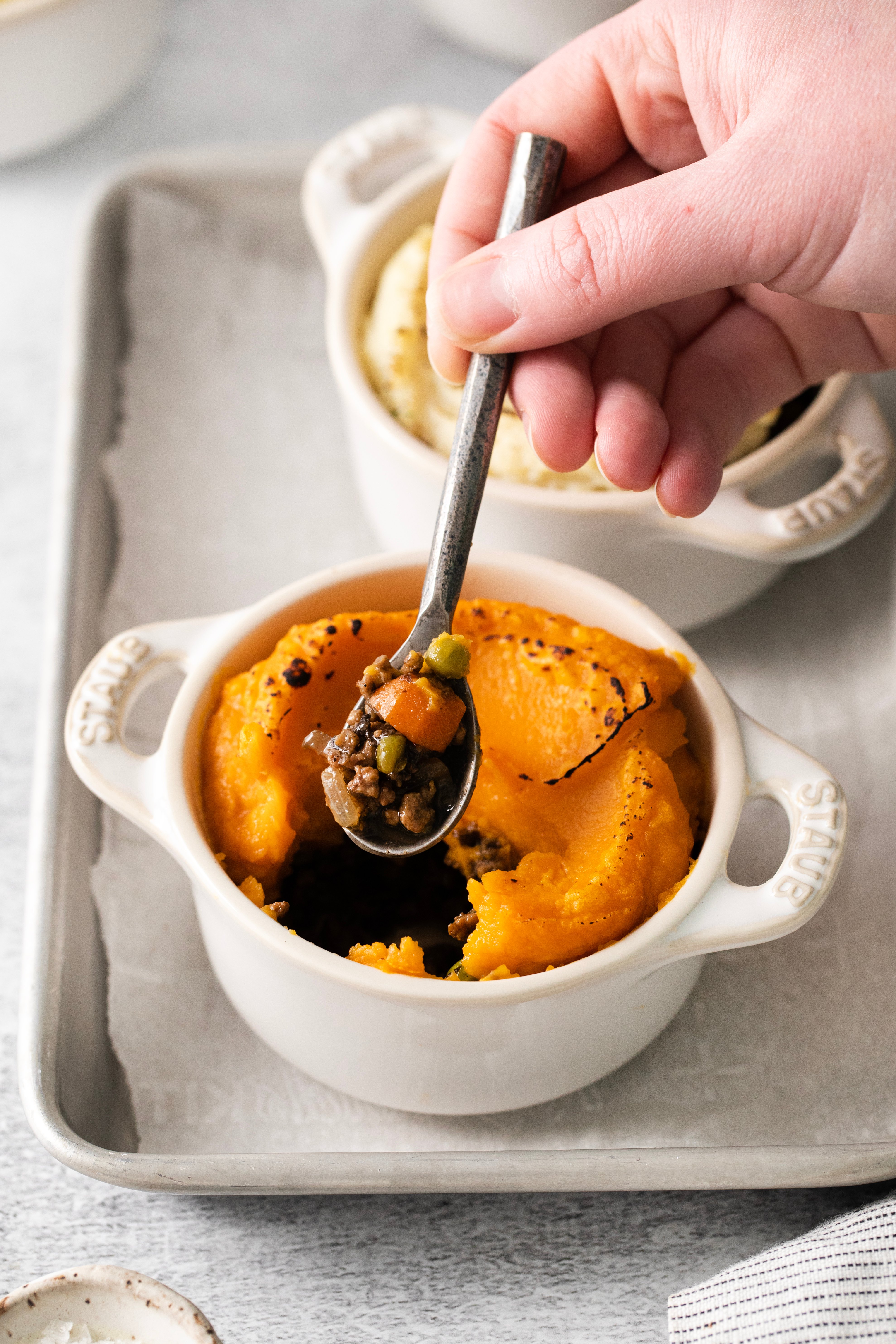 a spoon being plunged into a dish filled with sweet potato shepherd's pie.