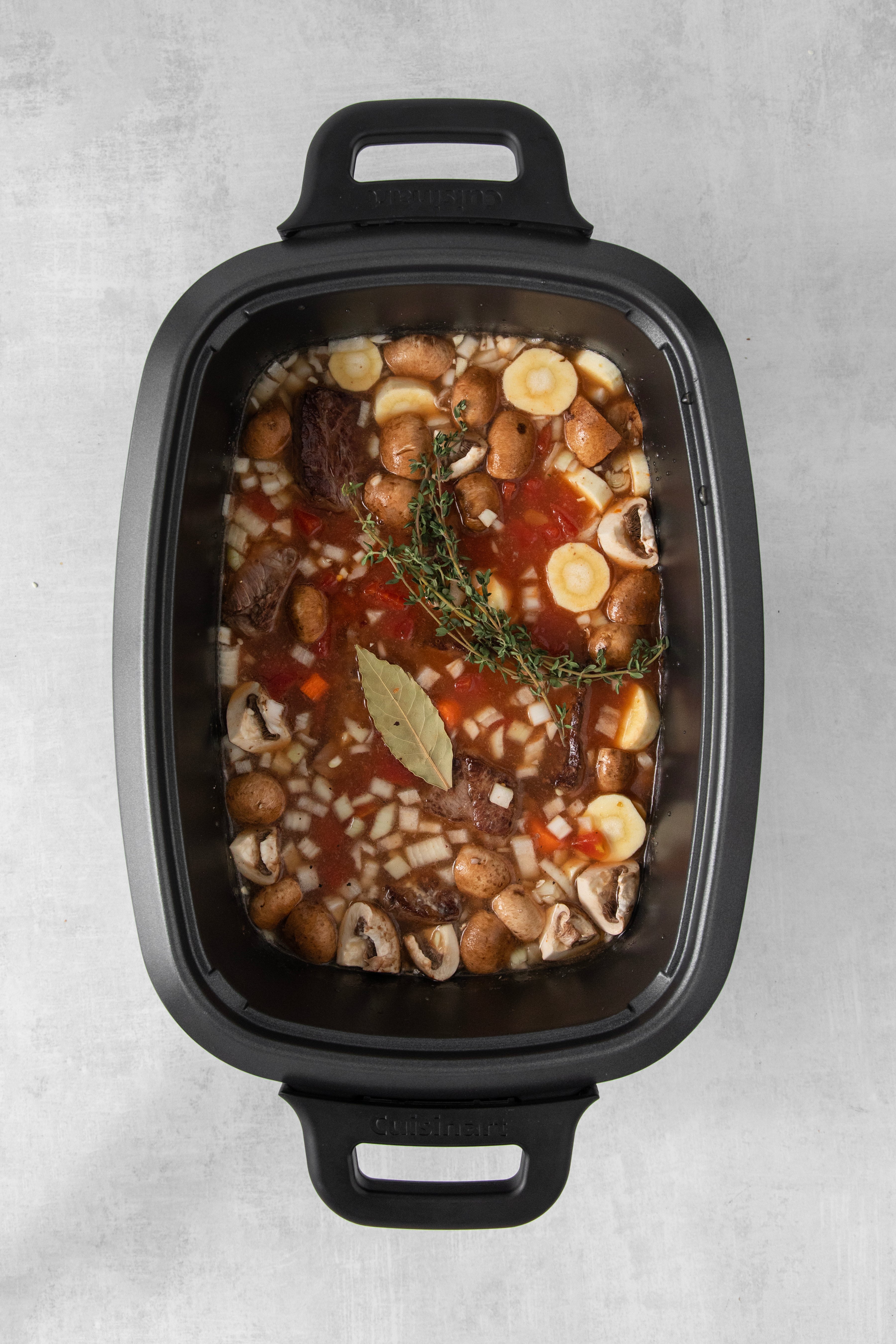 overhead of a slow cooker filled with beef stew ingredients.