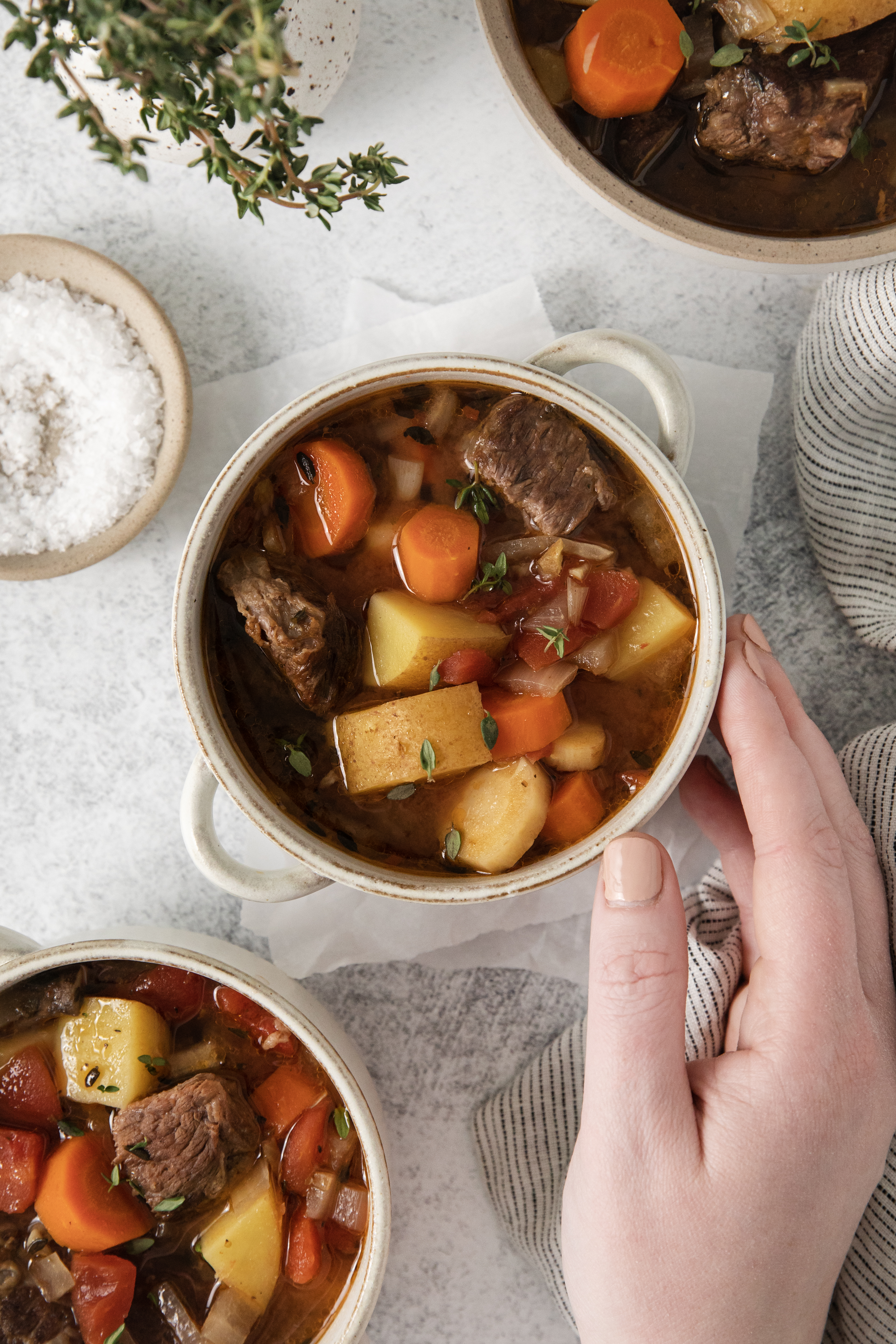 a hand touching a bowl of beef stew.