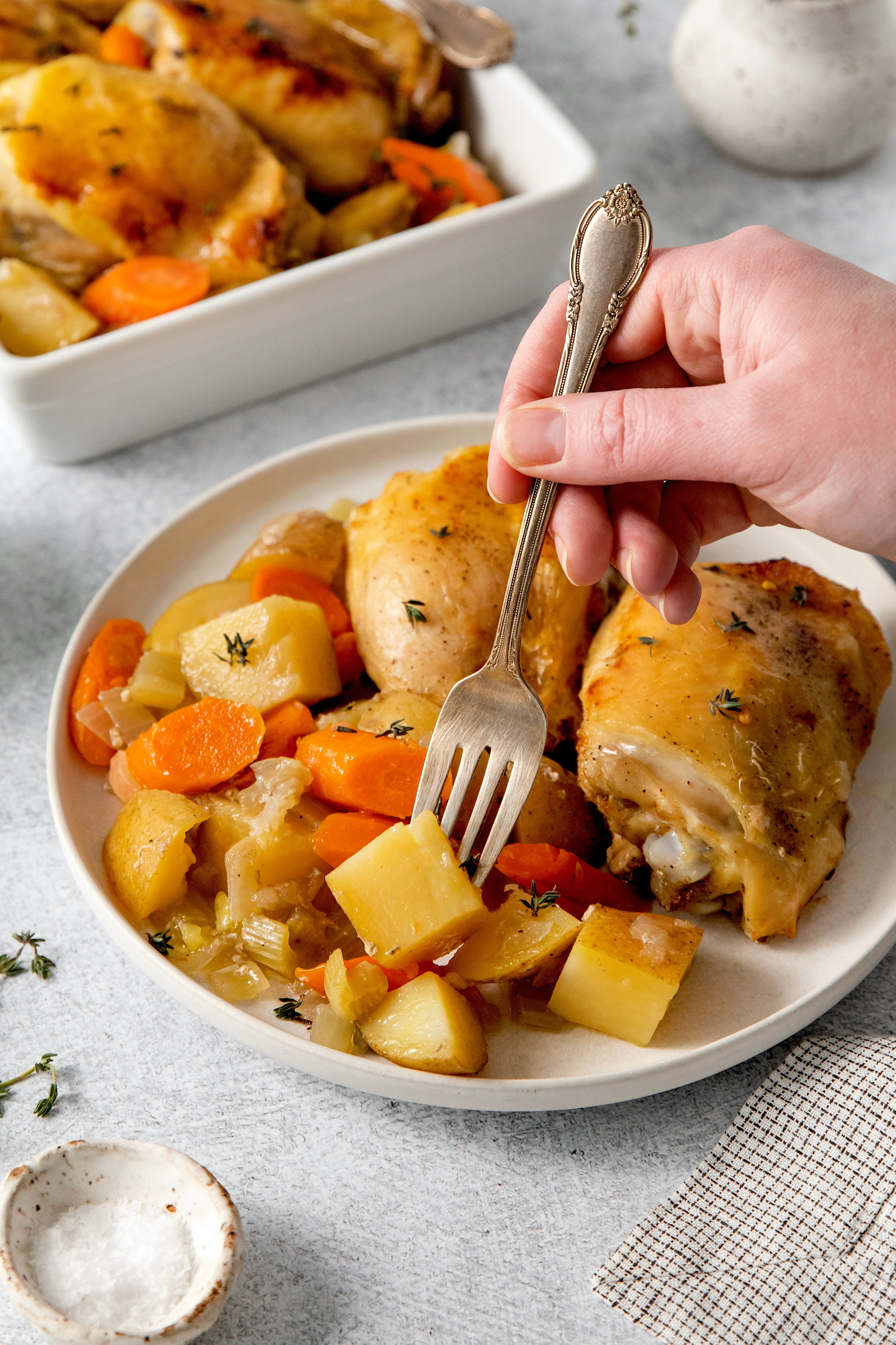 a fork picking up a potato on a plate filled with slow cooker chicken and veggie dinner.
