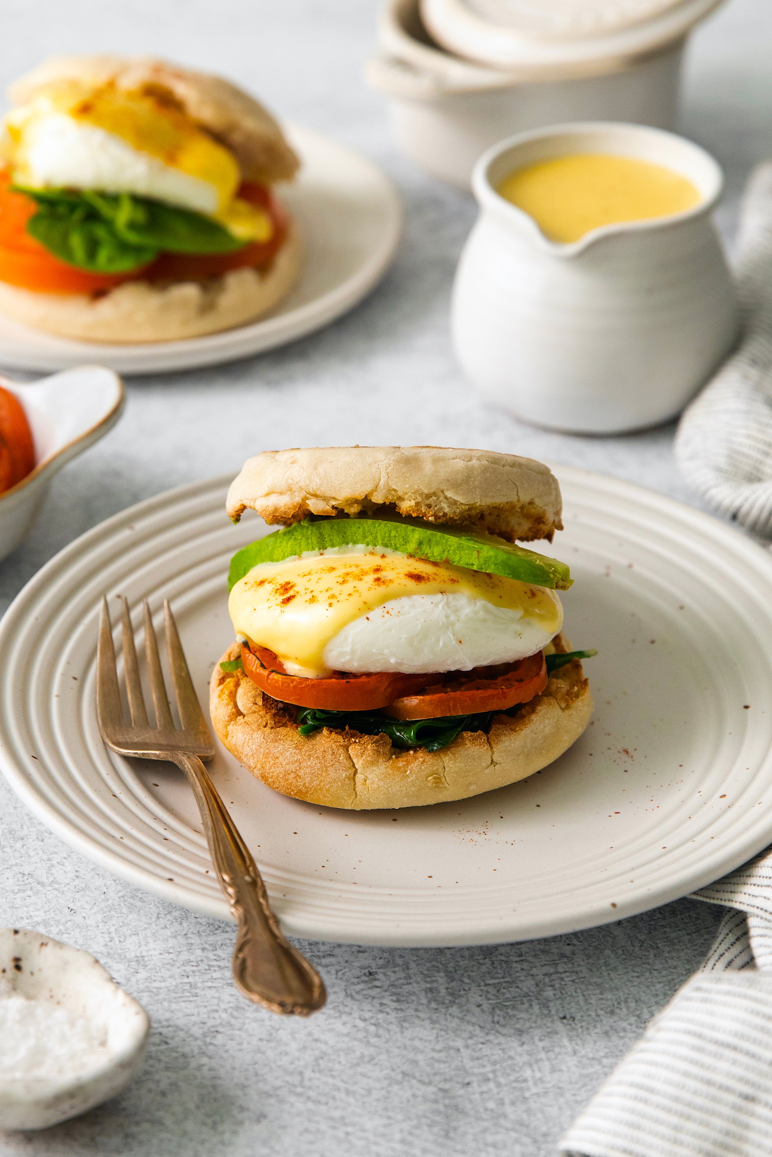 Side view of eggs Benedict sandwich assembled on a plate with a fork.