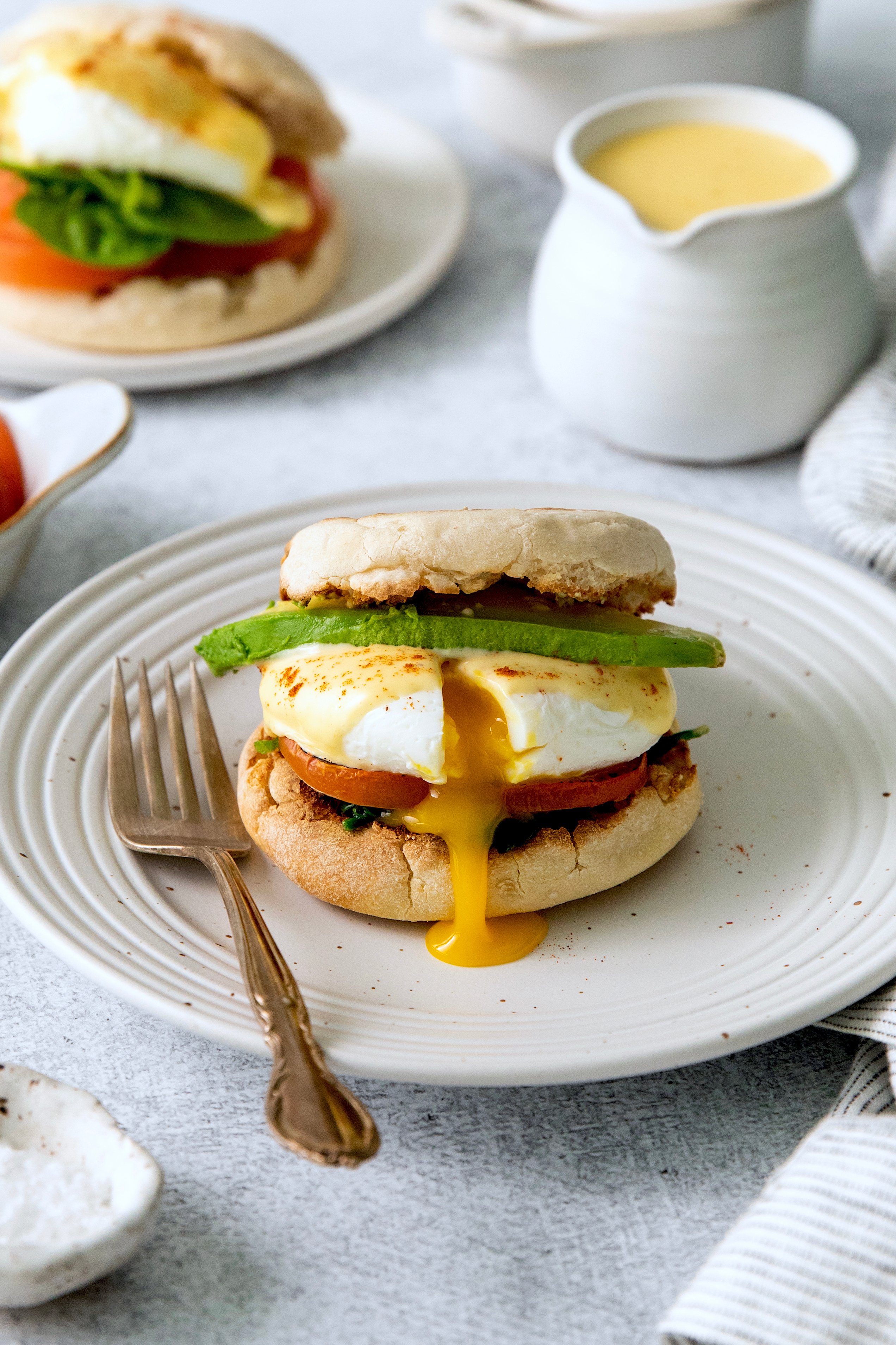 Side view of eggs Benedict sandwich assembled on a plate with a fork.