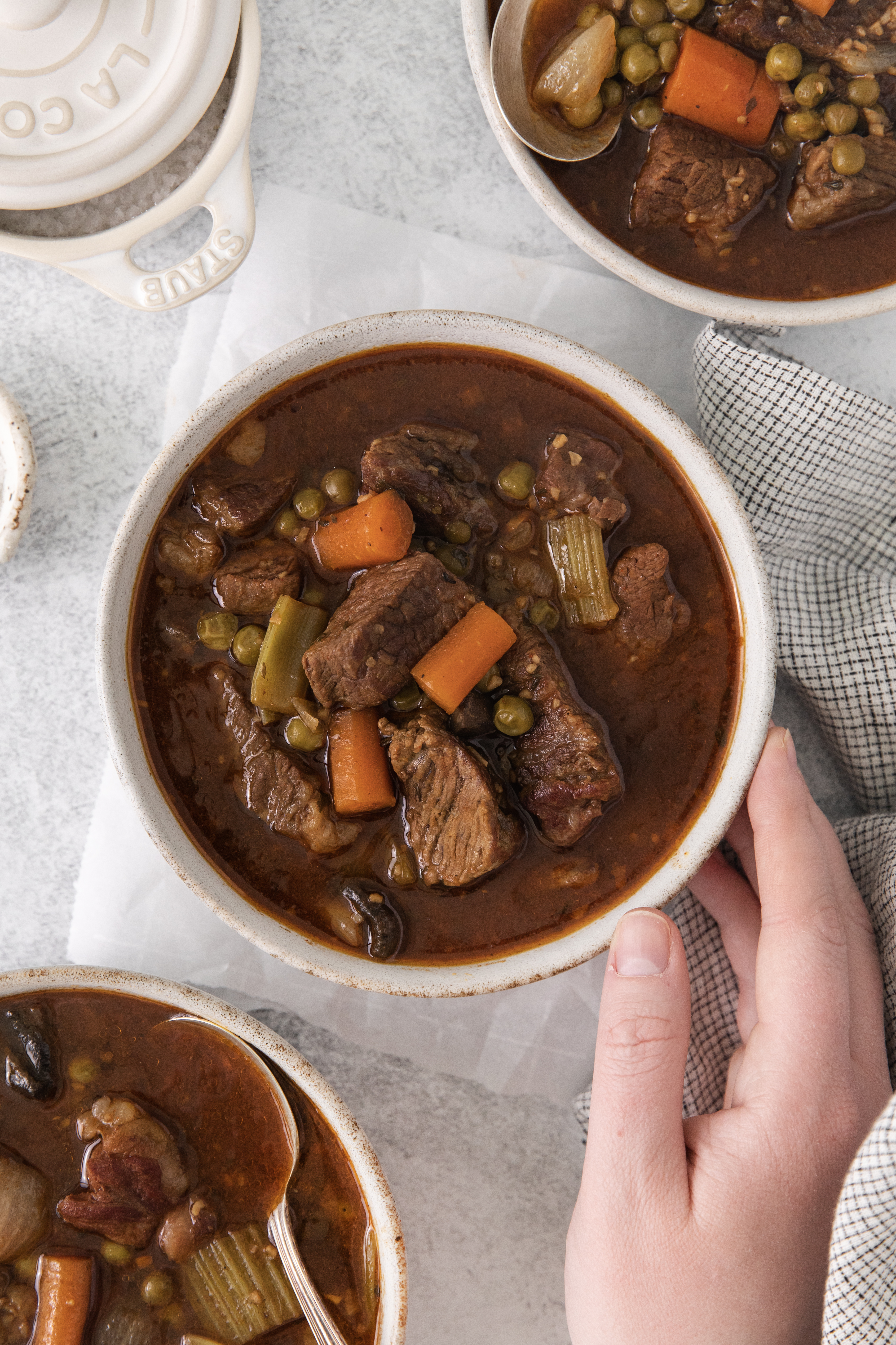 a hand touching a bowl of slow cooker beef and veggie stew.