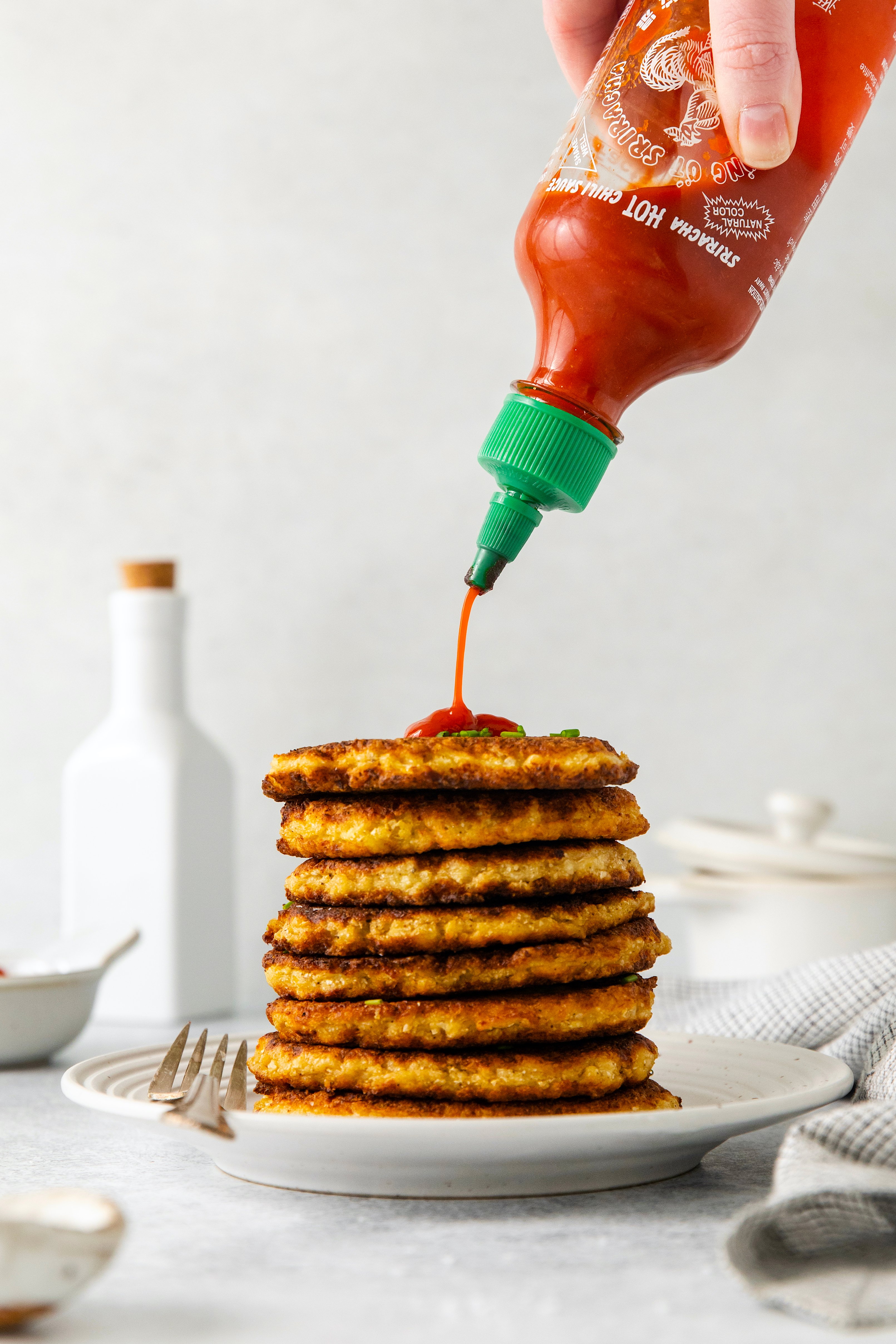 sriracha being drizzled on the top of a stack of hash browns.