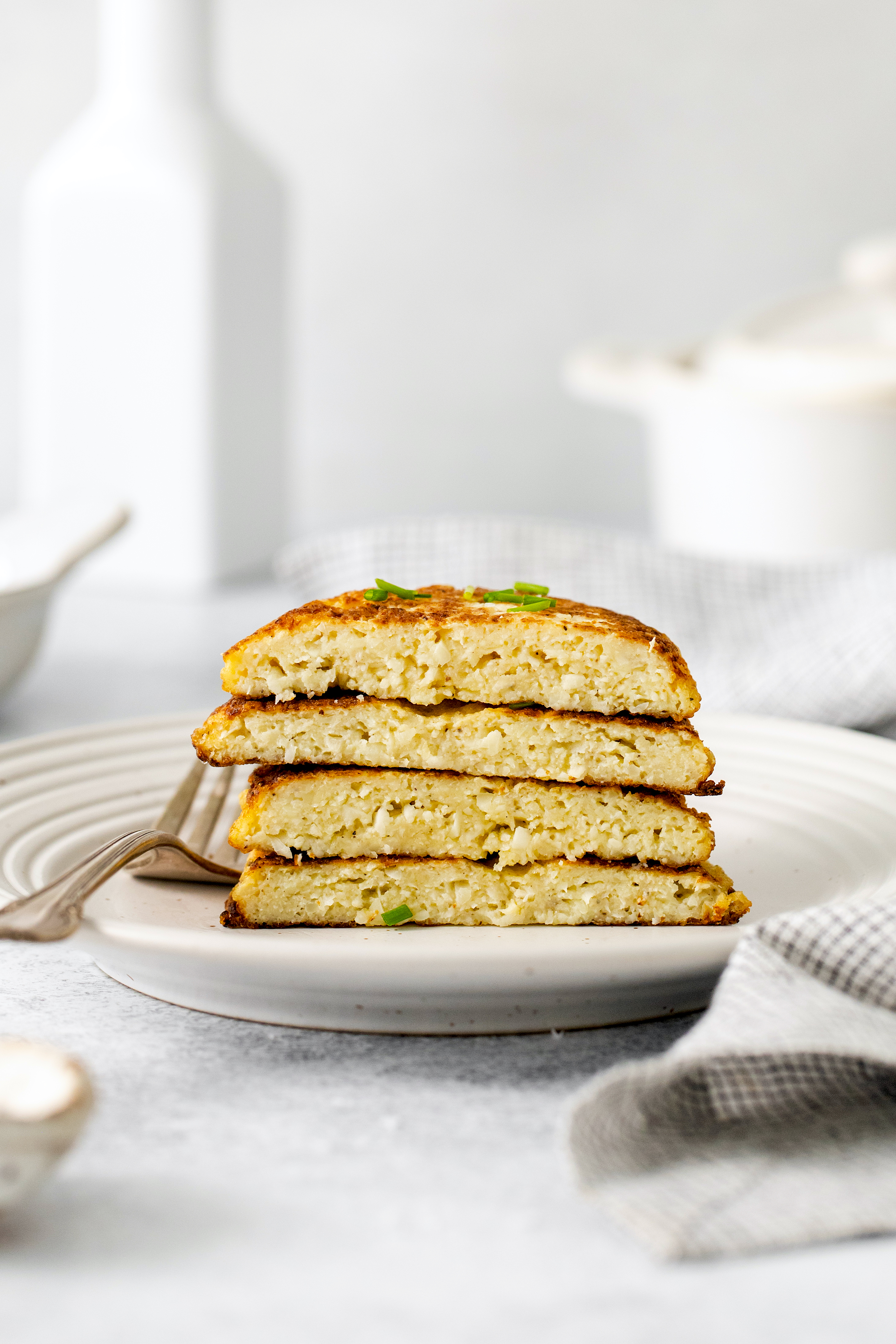 four halves of cauliflower hash browns stacked on a white plate.