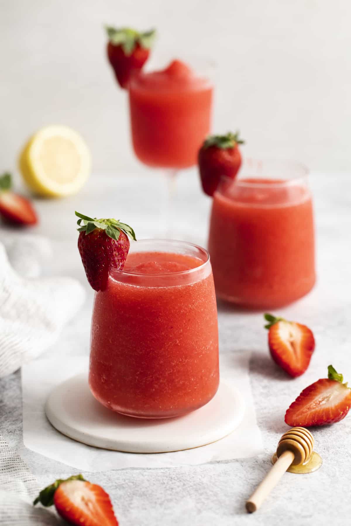 a glass of a wine slushy with another behind it garnished with strawberries.