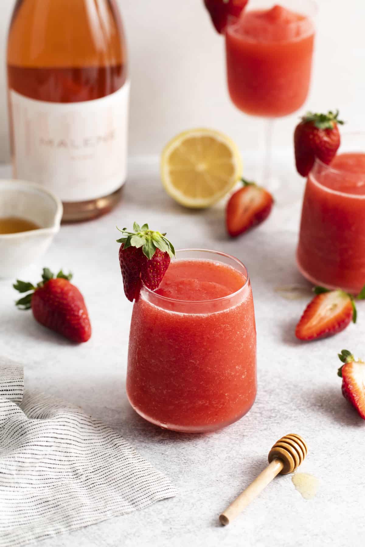 a glass filled with frosé surrounded by fresh strawberries and lemon.