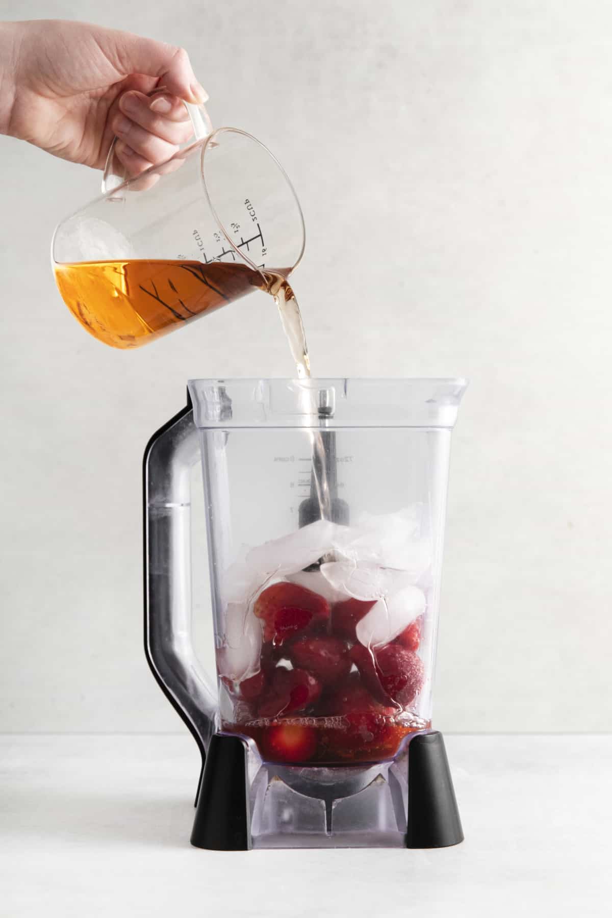 wine being poured into a blender with strawberries and ice.