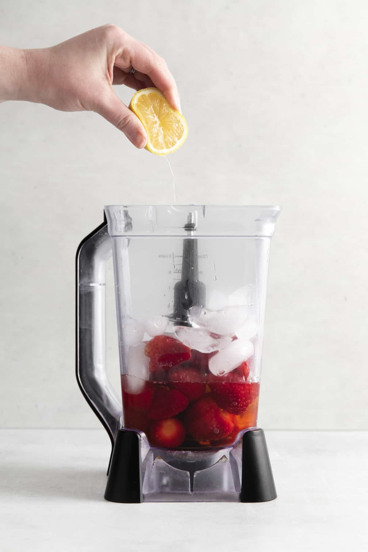 fresh lemon being squeezed into a blender with strawberries and ice.