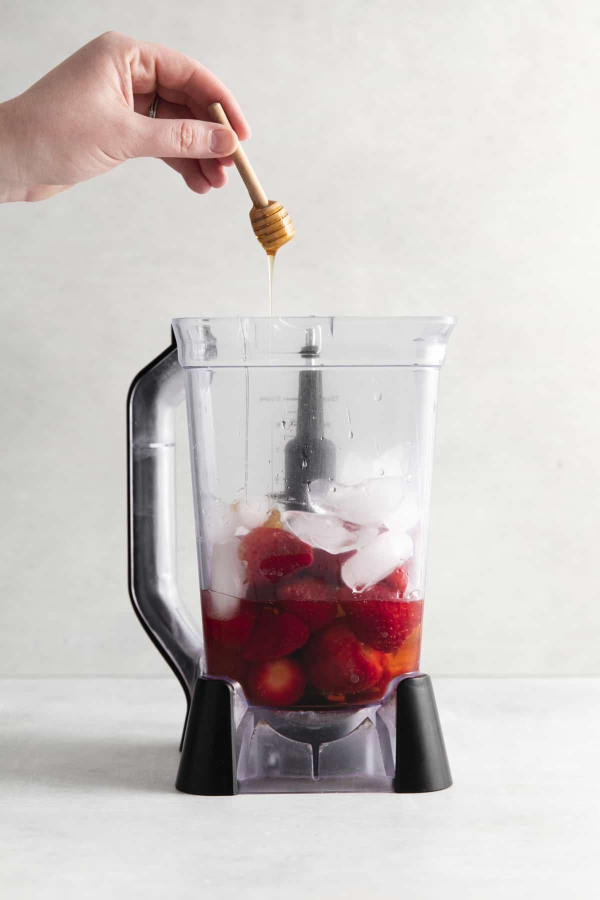 Honey is placed in a blender with strawberries and ice.