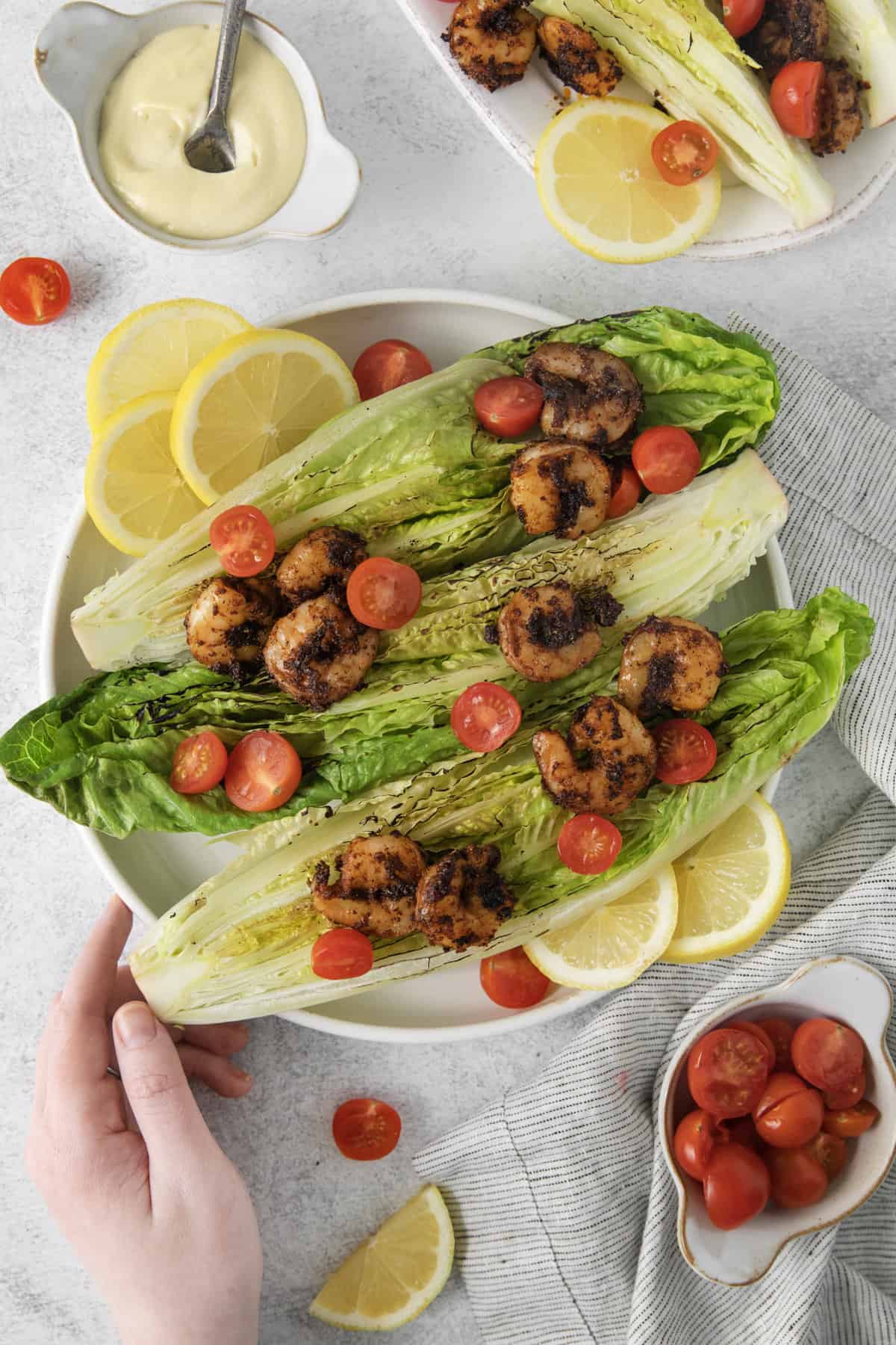 a hand touching a platter with grilled romaine salad.
