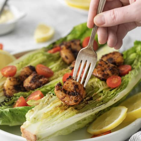 a piece of shrimp being lifted off of a grilled caesar salad.