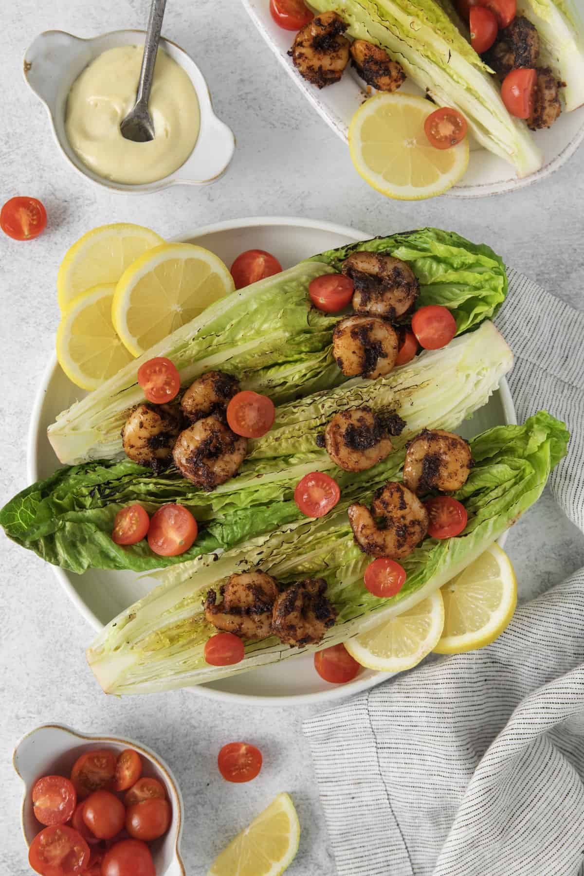 above shot of grilled lettuce topped with tomato and shrimp on a platter with lemon slices.