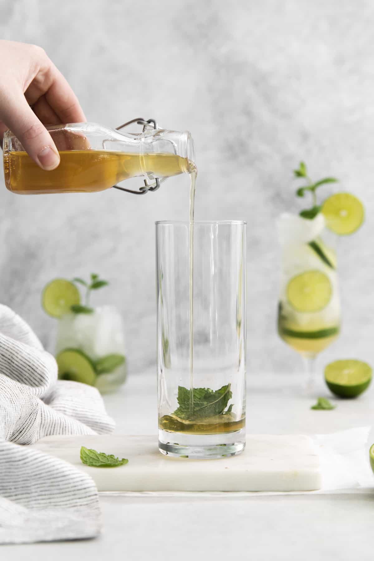 simple syrup being poured over mint leaves in a glass.