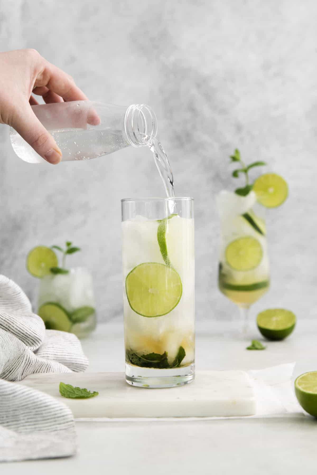 soda water being poured into a glass with mojito ingredients.