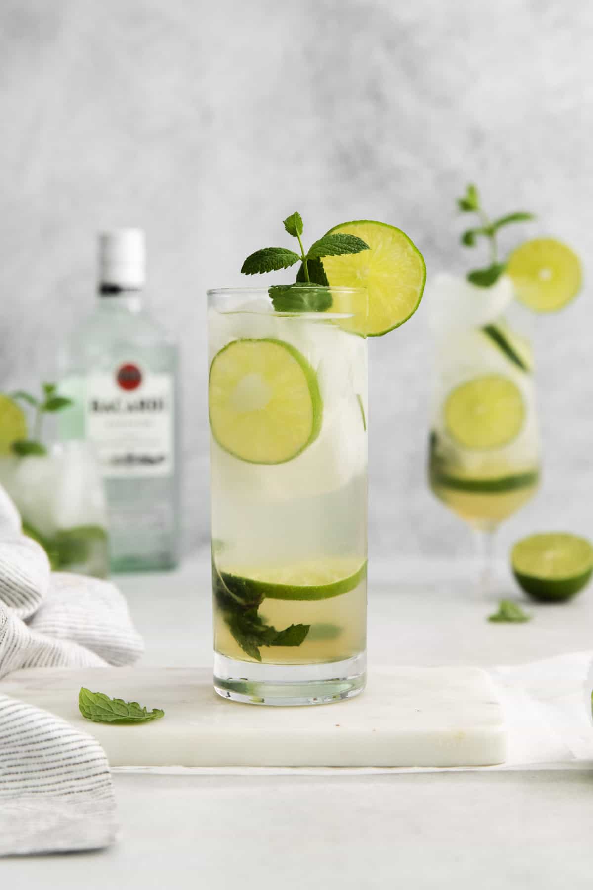 a mojito glass with another glass and a bottle of rum in the background.